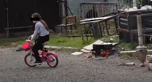 Ребенок в Степанакерте катается на велосипеде около костра, на котором взрослые готовят пищу. Стопкадр из видео https://www.youtube.com/watch?v=2Xp0RzSpu_U